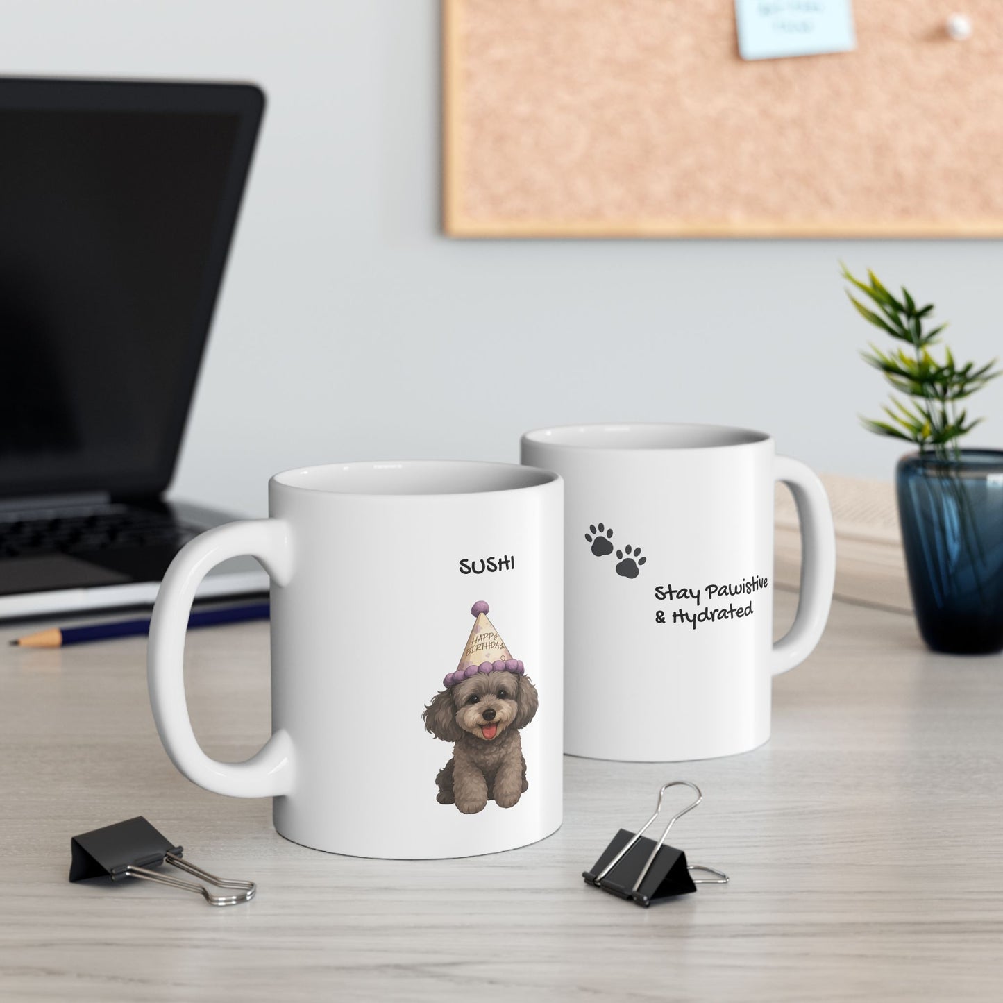 Two white mugs on a desk with a laptop and plant in the background